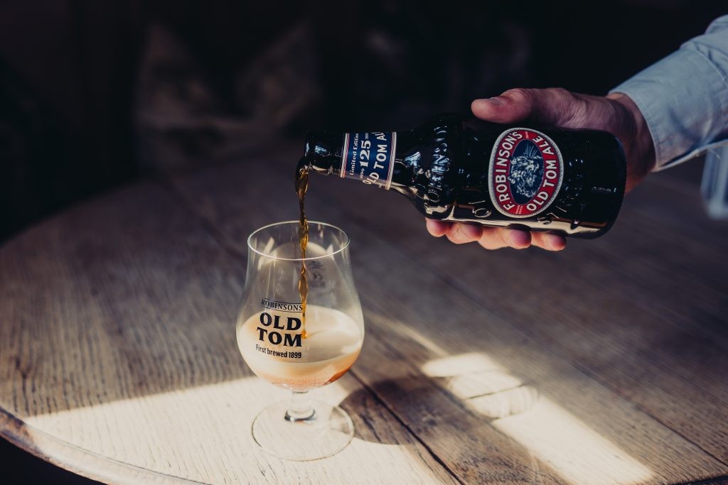 Hand pours Old Tom Beer Bottle into Old Tom Glass